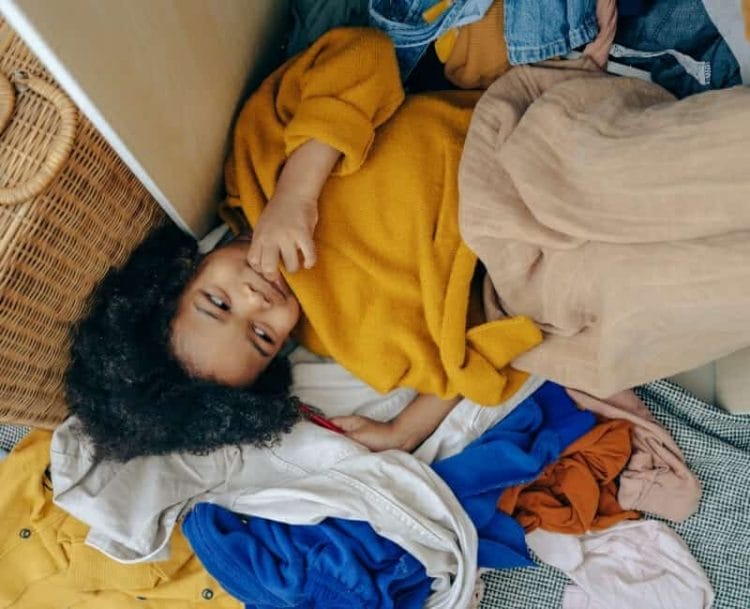 Too many clothes: Girl lying on floor with clothes piled on top of her