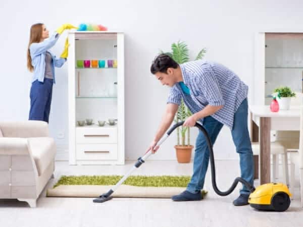 A list of household chores: Man vacuuming and woman dusting shelves